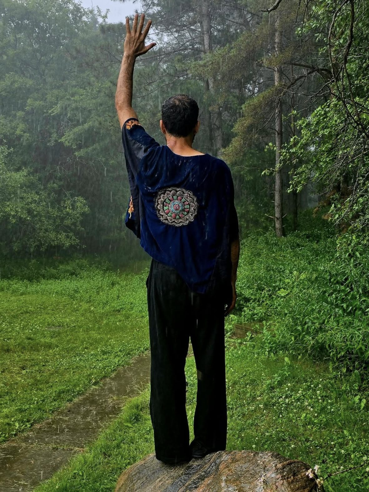 Kamakan artist in an outdoor portrait, arm raised in the rain